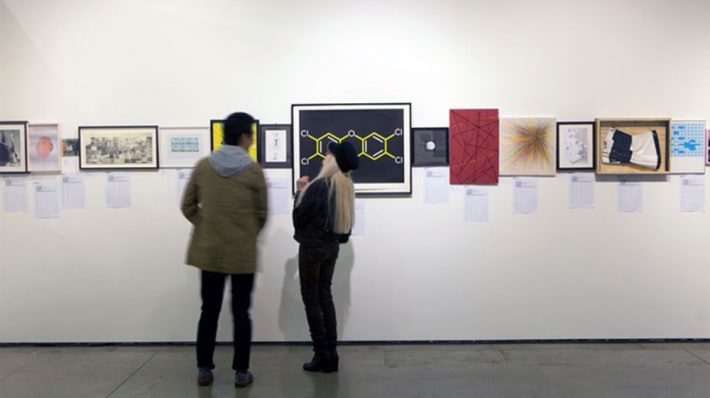 People looking at donations to the Postgraduate Art Auction on display in the Lethaby Gallery
