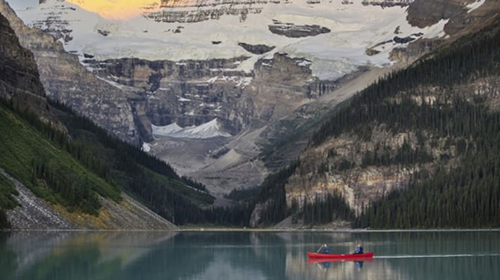 Photo of a red canoe with two people in on the water of Lake Louise in Aberta, Canada with mountains surrounding