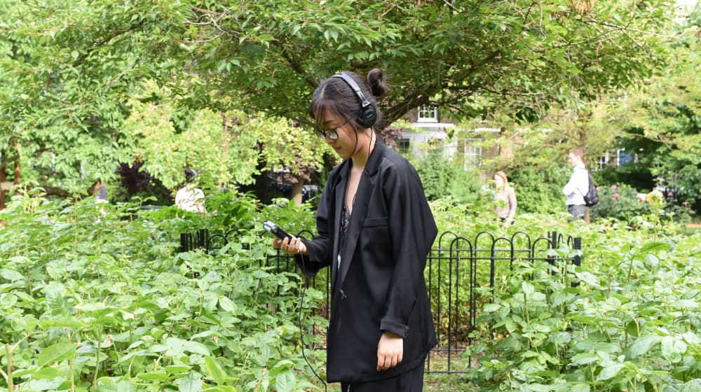 Woman walking through a garden wearing headphones looking at her phone