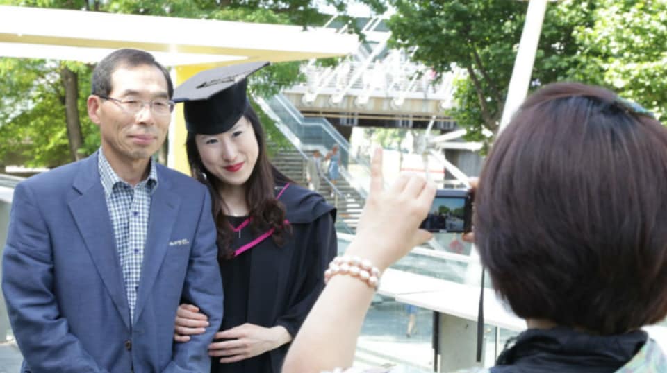A graduate in their graduation gown having a photo taken with their parents.