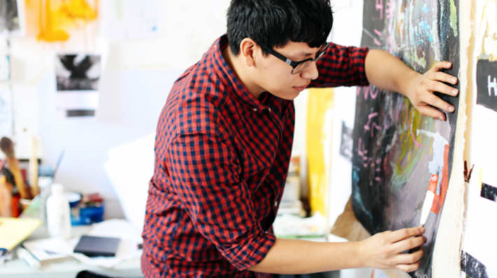 Photo of a man working on a piece of art hanging on a wall