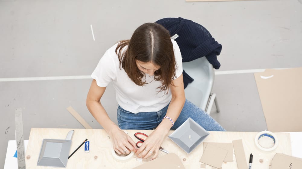 View down to a student seated at a desk and using various tool and cardboard materials.
