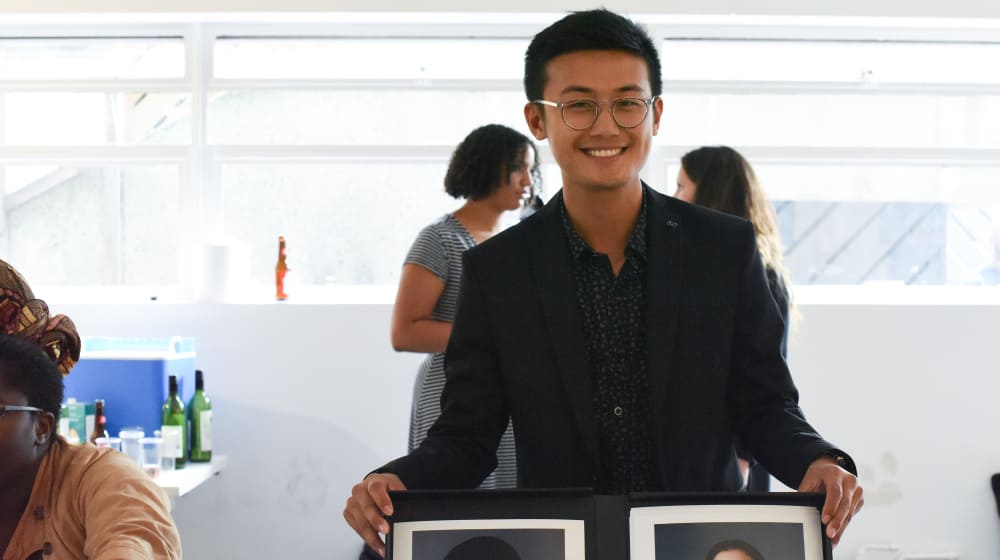 Image of Student Calvin Ma with his photographic work holding two frames in his hands.