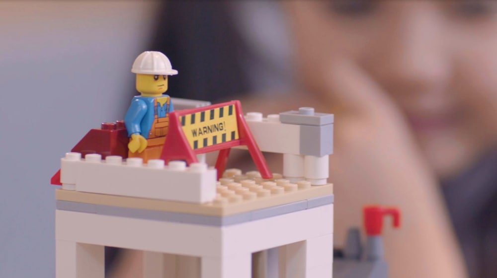 Close up still from a film. Lego tower with a lego construction worker.