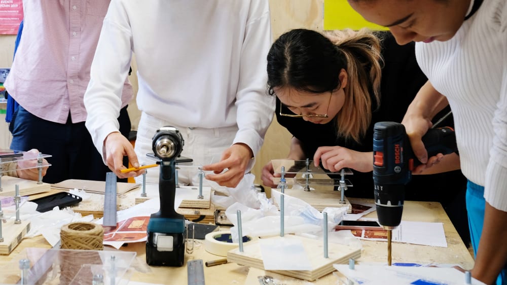 Group hover over workbench working on a wood piece