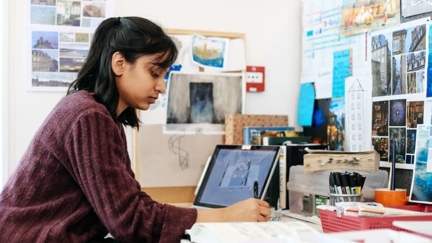 Person at a desk using a laptop and creating artwork