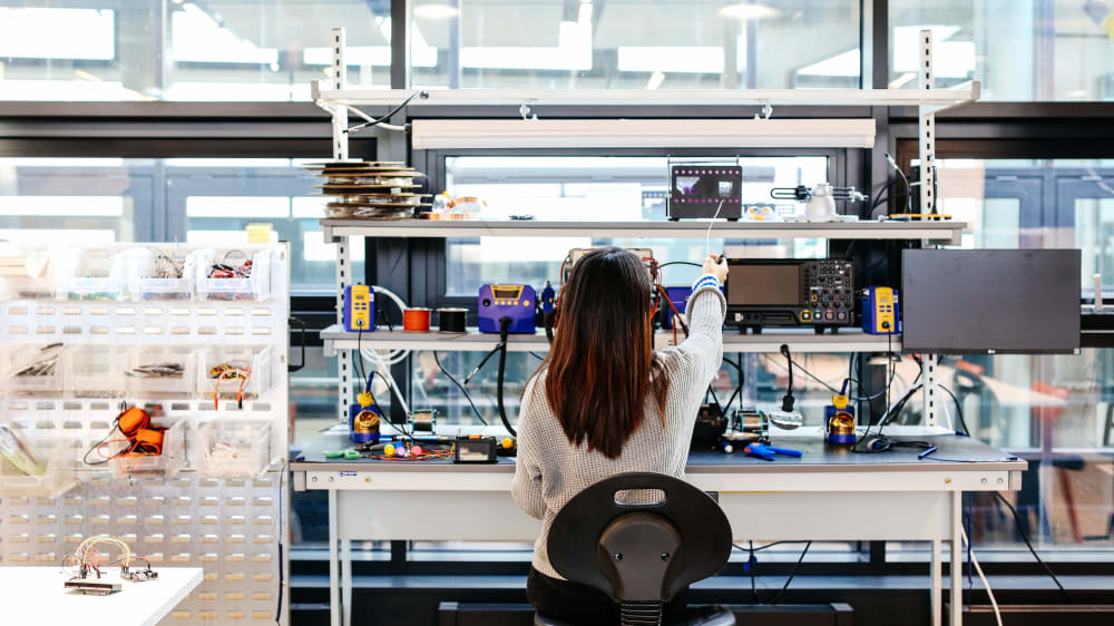 A student working at a desk surrounded by electronic equipment