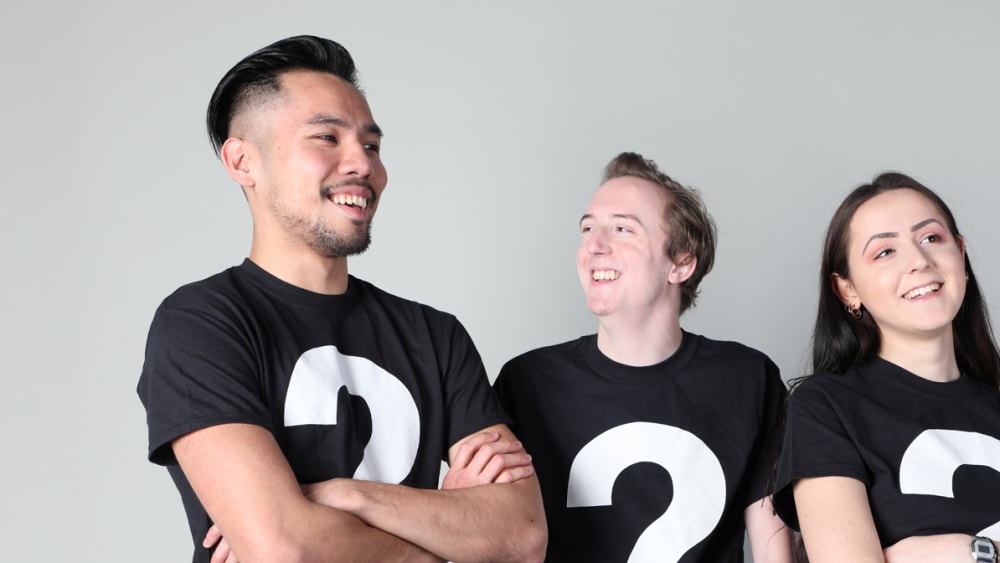 Image of 3 students, 2 male and 1 female wearing black t-shirt with white question marks.