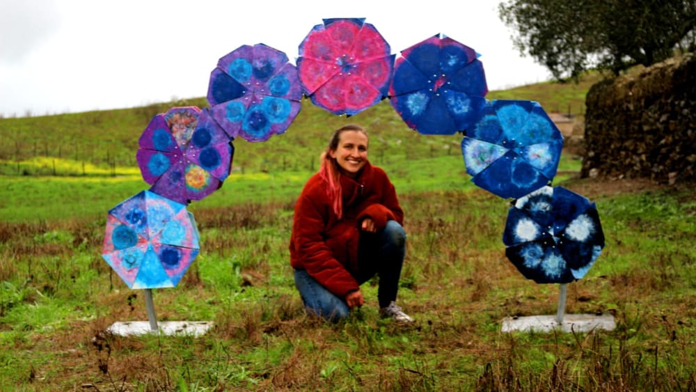 woman squatting in a field under a plastic sculpture