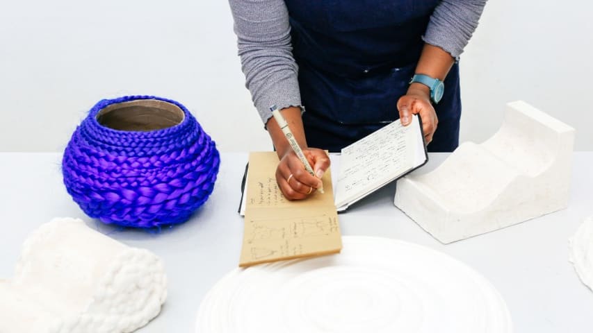 Student writing in a notebook with her sculptures