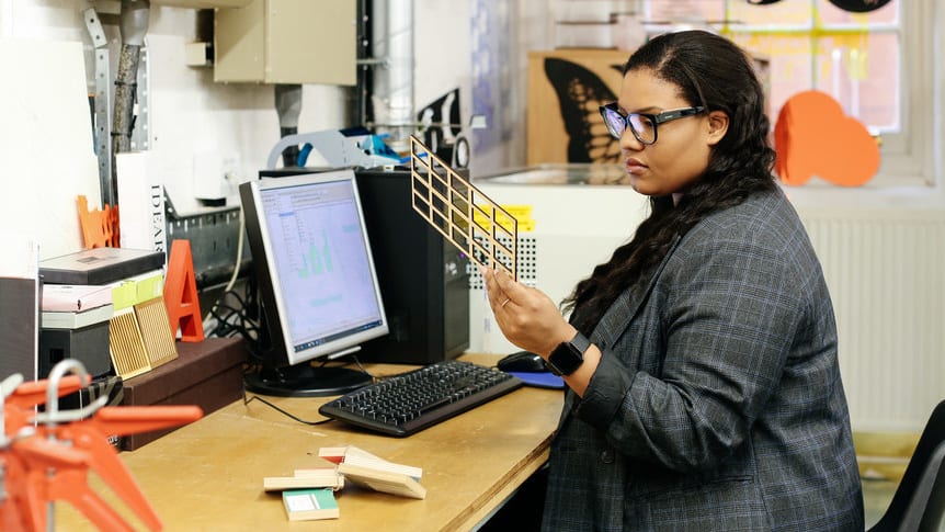Woman looking at 3D printing and sitting at a desk.