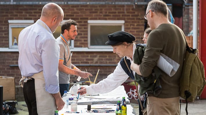 Photo of a group of people at a table outside using paintbrushes