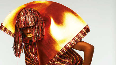 Person in a shiny wig posing in a striped outfit with a huge collar fanning out the back