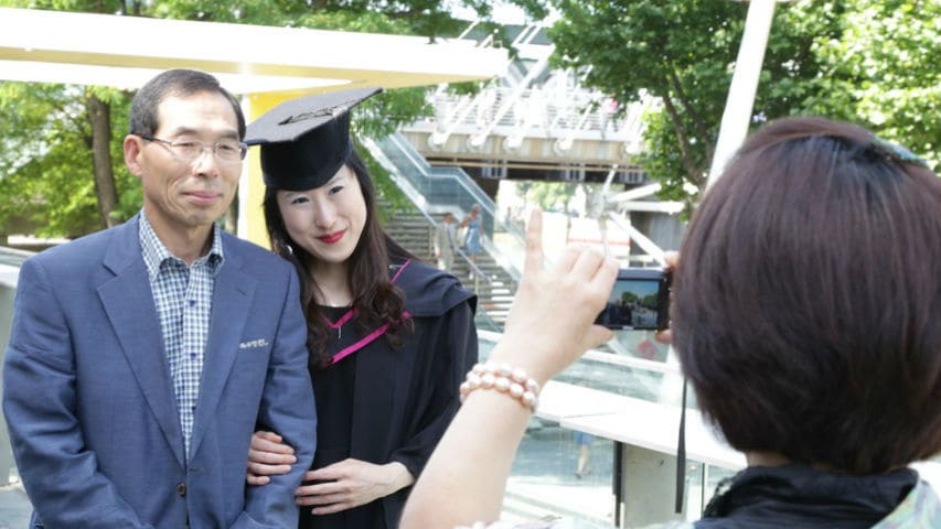 A graduate in their graduation gown having a photo taken with their parents.