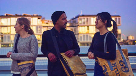 Three people of a rooftop wearing bags created from recycled packaging