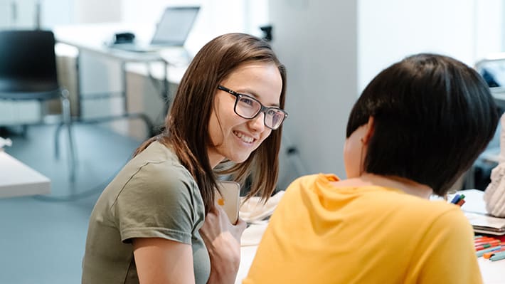 A woman wearing specs advises a person in yellow. They are sitting at a desk.