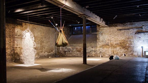 Photo of a large room with brick walls with a brown sack hanging from a beam and a white sculpture