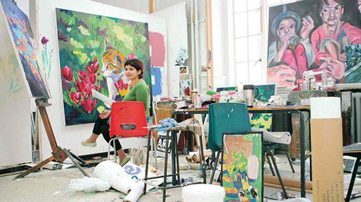 A painter in her studio looking to camera