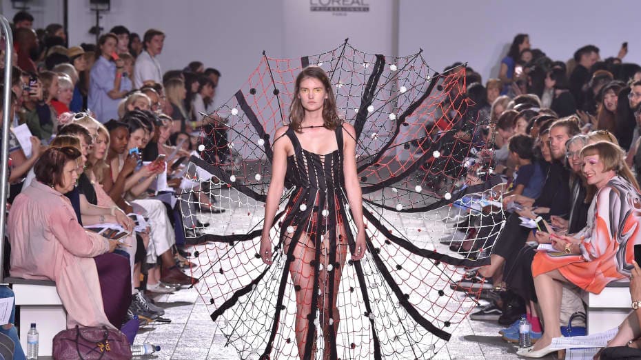 A model walking down a catwalk wearing a very detailed garment the bottom of which splays out like a spider's web.