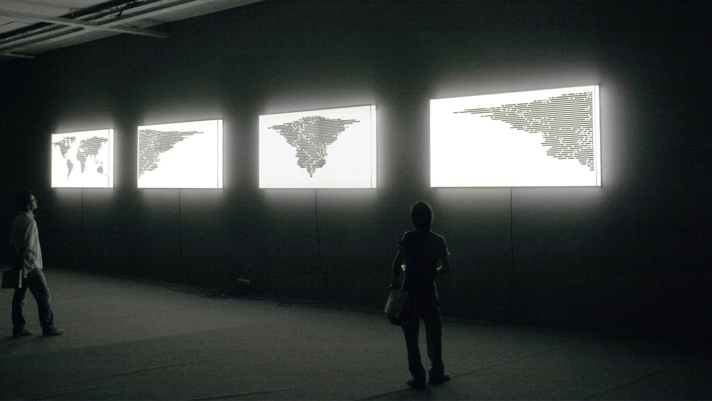 People looking at an art installation of light boxes with world maps printed on them