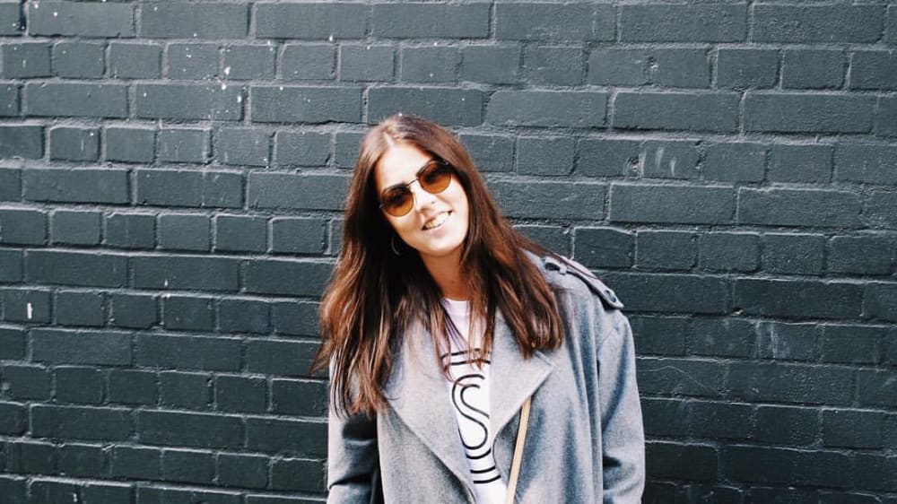 Natalie Grogan in front of a wall, wearing sunglasses