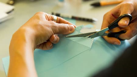 Close-up photograph of a someone cutting through some light blue paper
