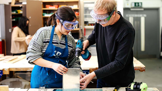 A technician assisting a student with a hand drill in the 3D Workshop.