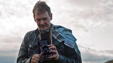 A picture of a man standing outside holding a vintage camera.