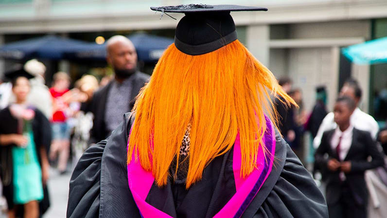 Student in full graduation robes walking towards the Royal Festival Hall