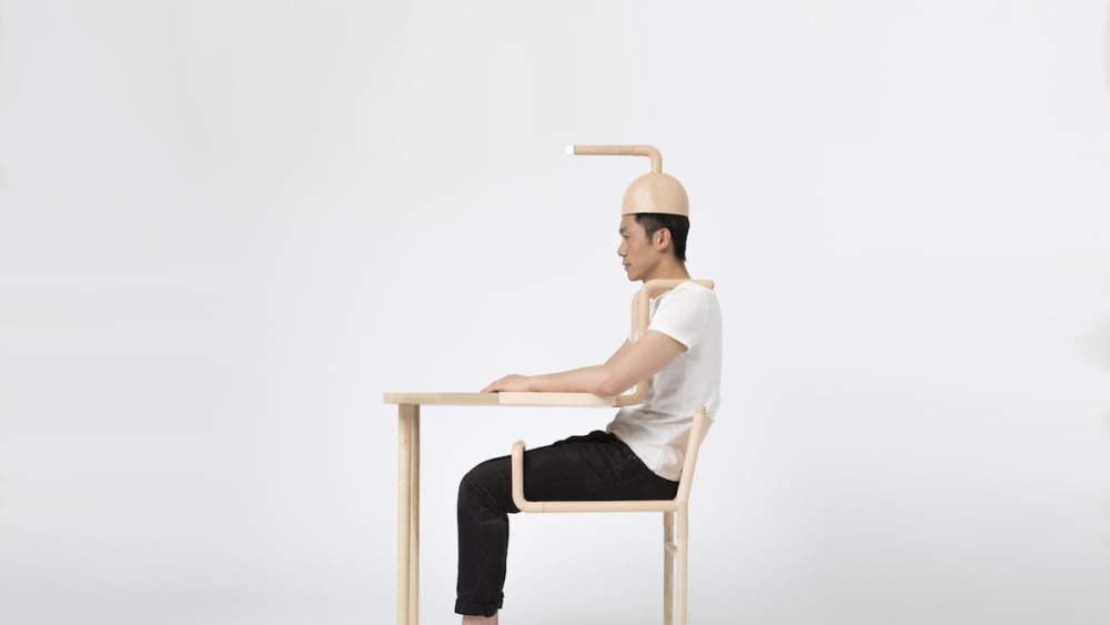 Photo of a man sitting at a table with a round wooden hat on with a pipe coming out of the top