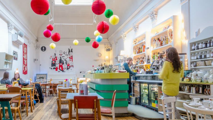 An airy room filled with tables and chairs surrounding a bar, brightly coloured lanterns hang from the ceiling