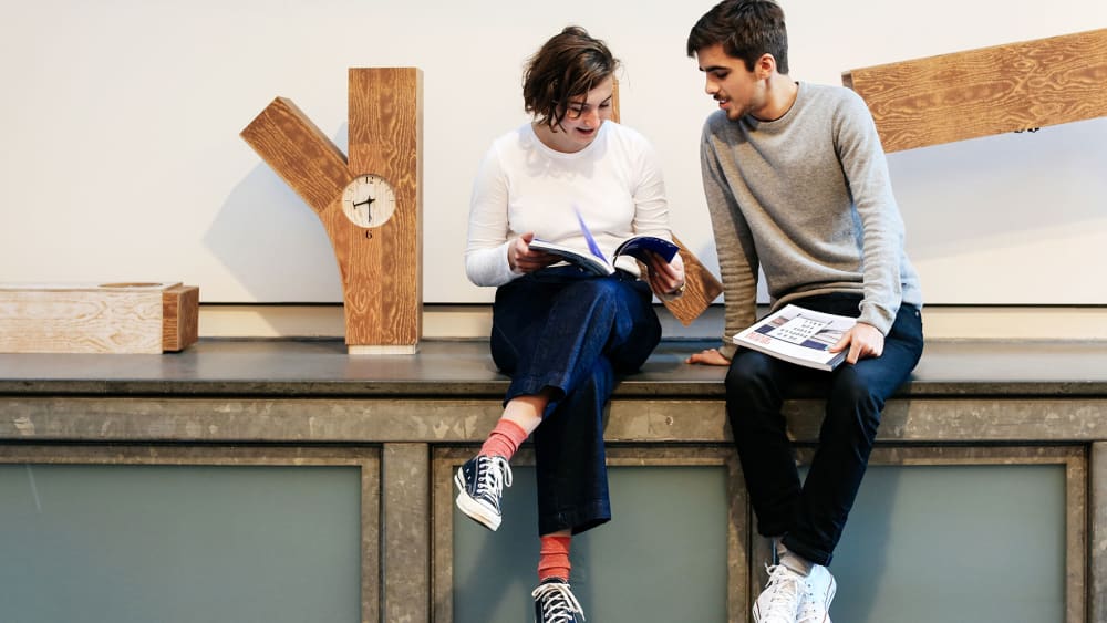 Two students sitting on a ledge near a clock