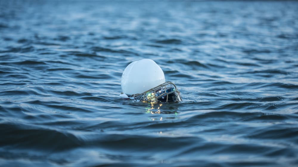 A blue sea in which what looks like a small white buoy with electronics floats