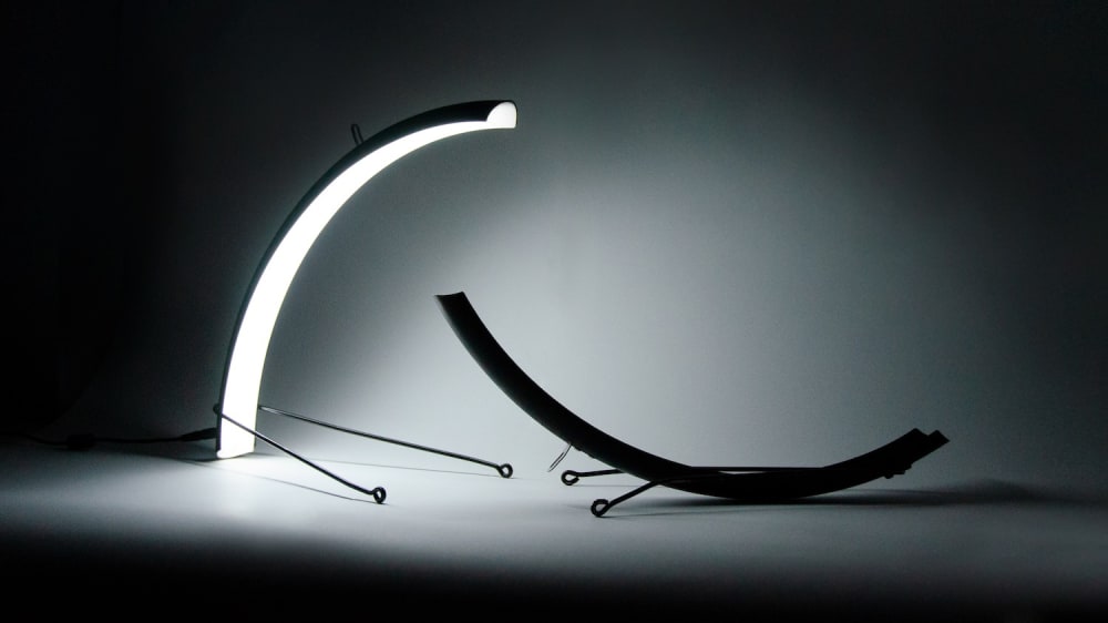 Two curved forms that may be lighting fixtures shine in a darkened space