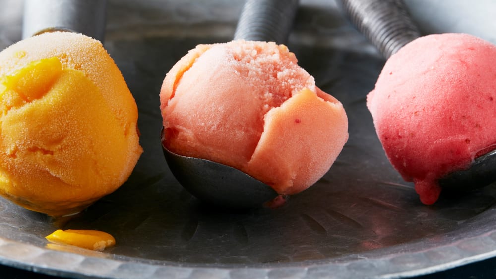 Three ice cream scoops side by side each holding with a different colour sorbet