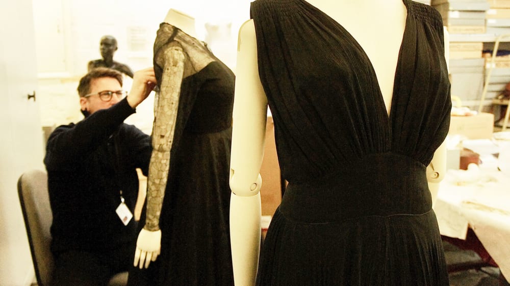 Curator dressing 2 mannequins with evening dress