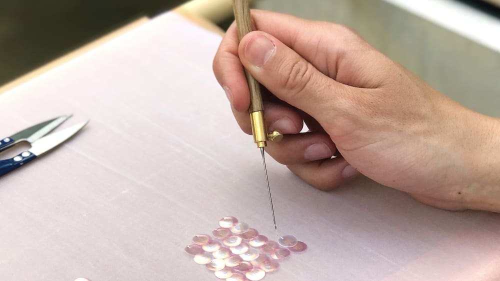 A hand is seen stitching pink sequins onto a fine pink gauze