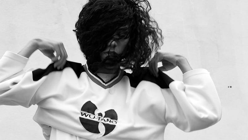 A girl putting on a jumper with 'Wu-Tang- logo