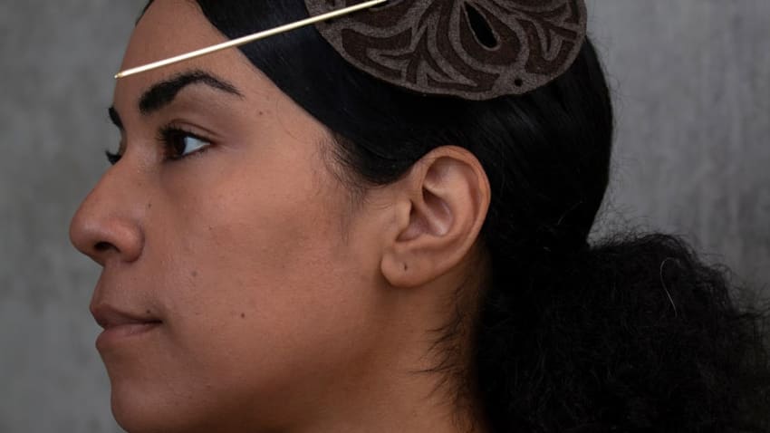 A model wearing a hairpiece consisting of a brown circular object with a long pin through it