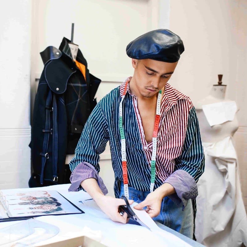 A person with a measuring tape around their neck cuts fabric.