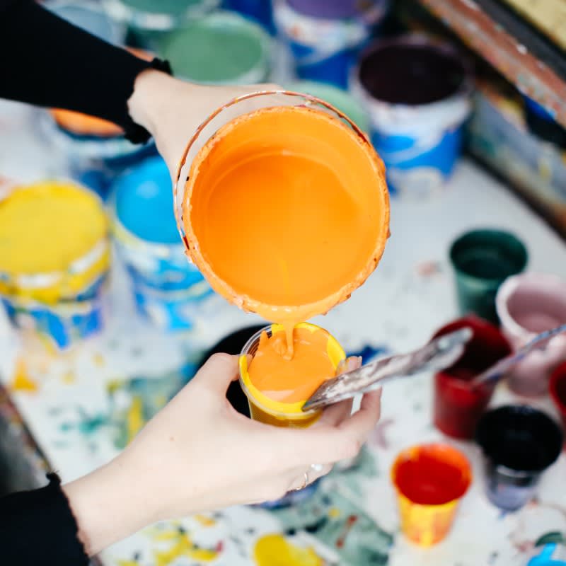 Orange paint being poured into a pot.