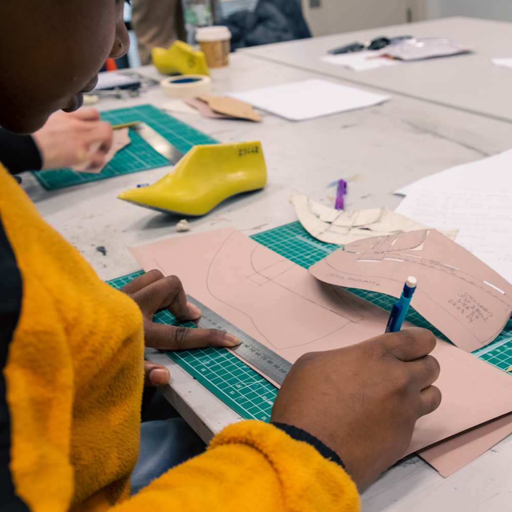 Student working on a shoe pattern, holding a ruler and a pencil