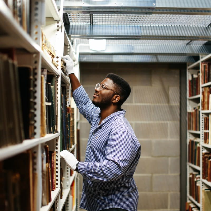 A person in a library reaches up to take a book off the shelf.