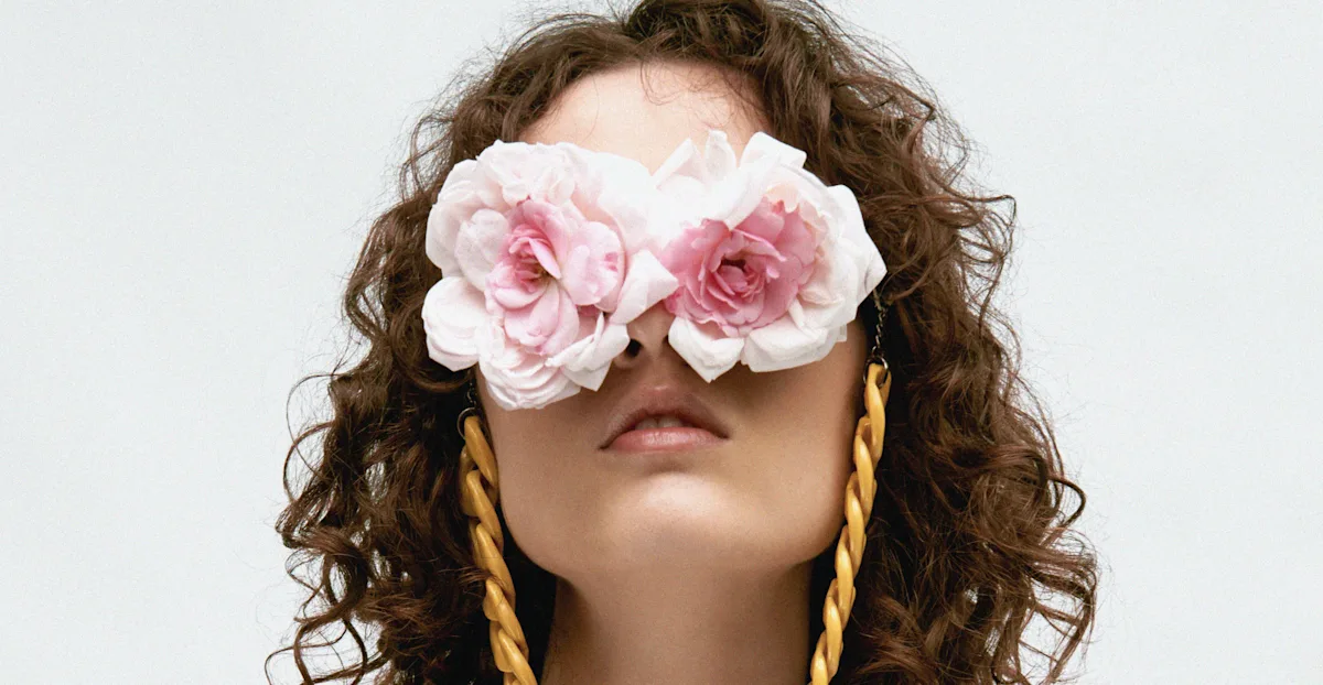 Female model in white dress with rose petals on her eyes.