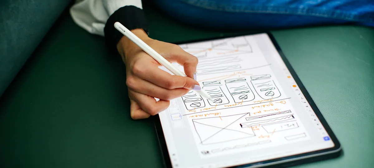 Photograph of someone taking notes on an ipad, against a green sofa.