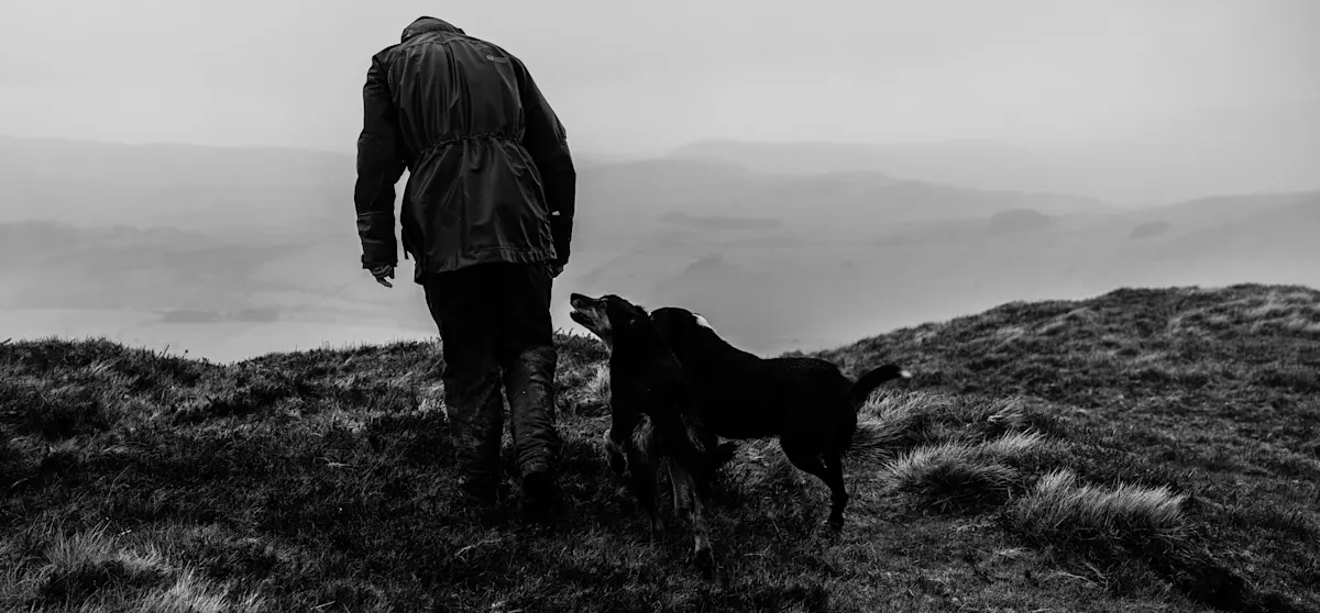 Black and white photograph of a man on a cliff walk with his collie dog.