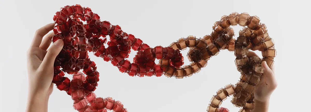 Two hands holding up a red-coloured interlinked piece of jewellery.