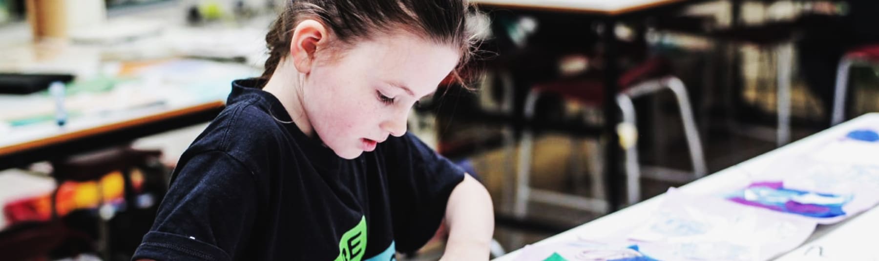 A young girl sticking down brightly coloured cut out shapes to a long piece of paper.