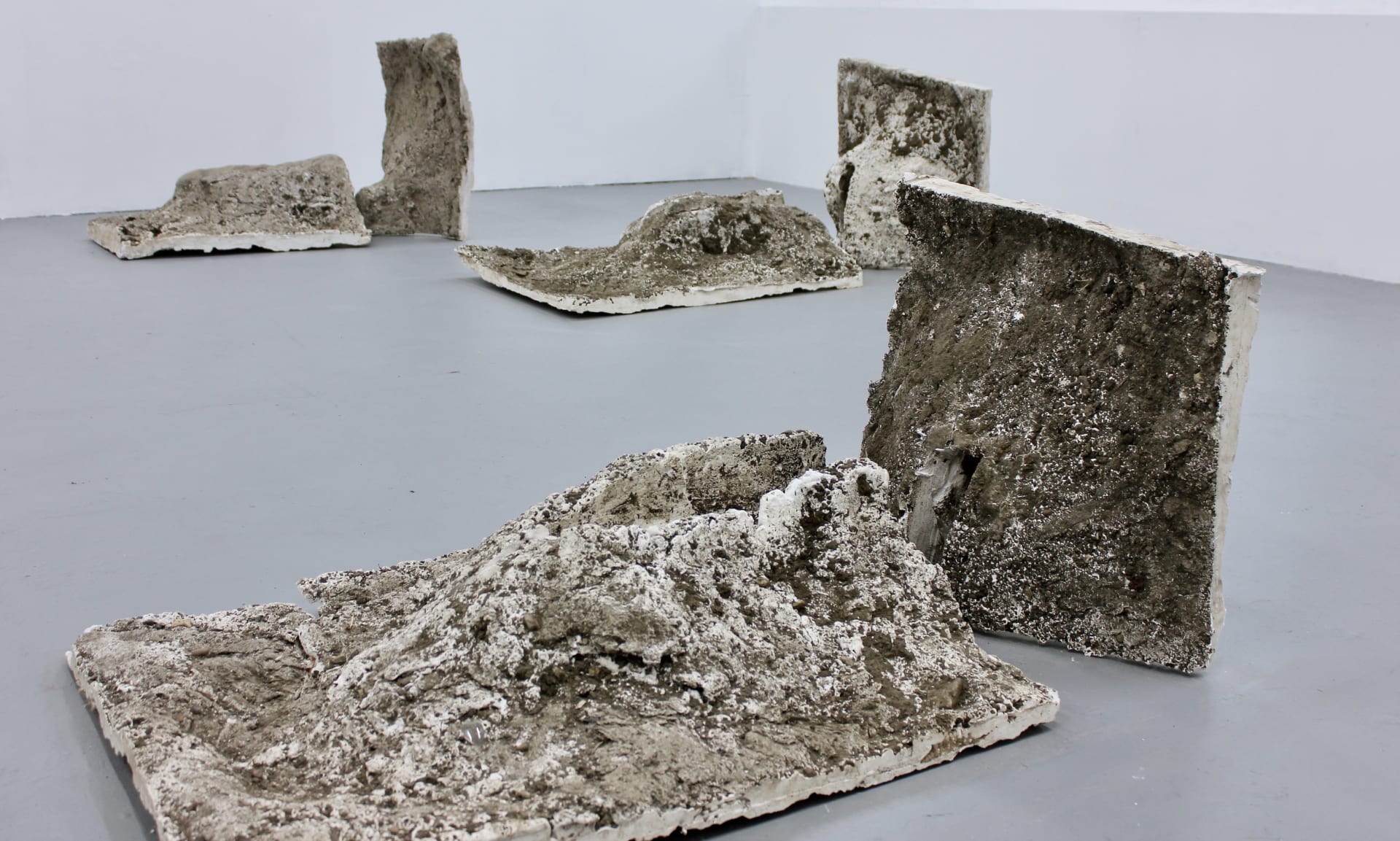 Three staggered sculptures made of plaster that was cast in a dirt hole. Each of the sculptures consists of two parts, one upright and one lying down.