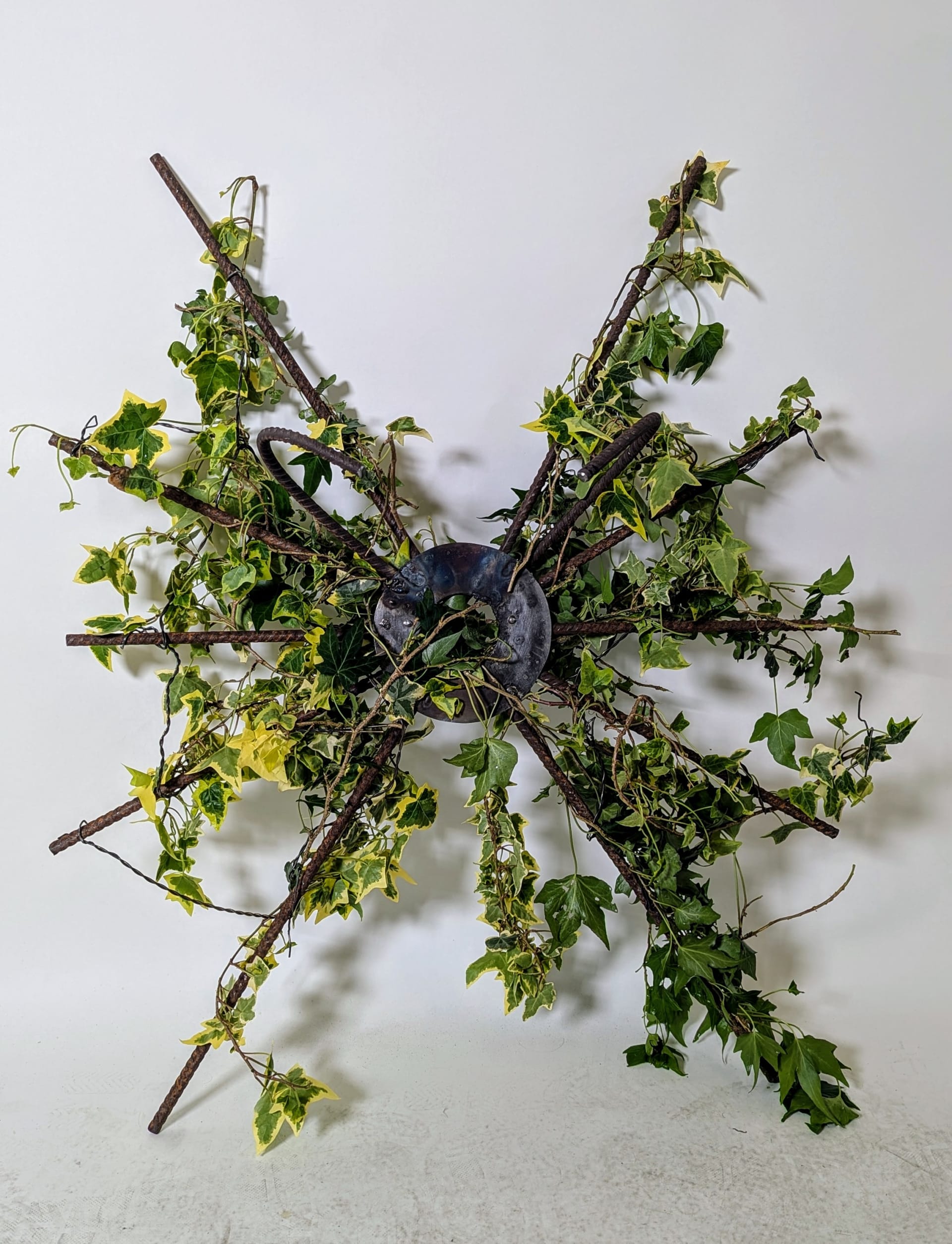 a large radial sculpture made of rusted metal rebar adorned with ivy and weathered wires.